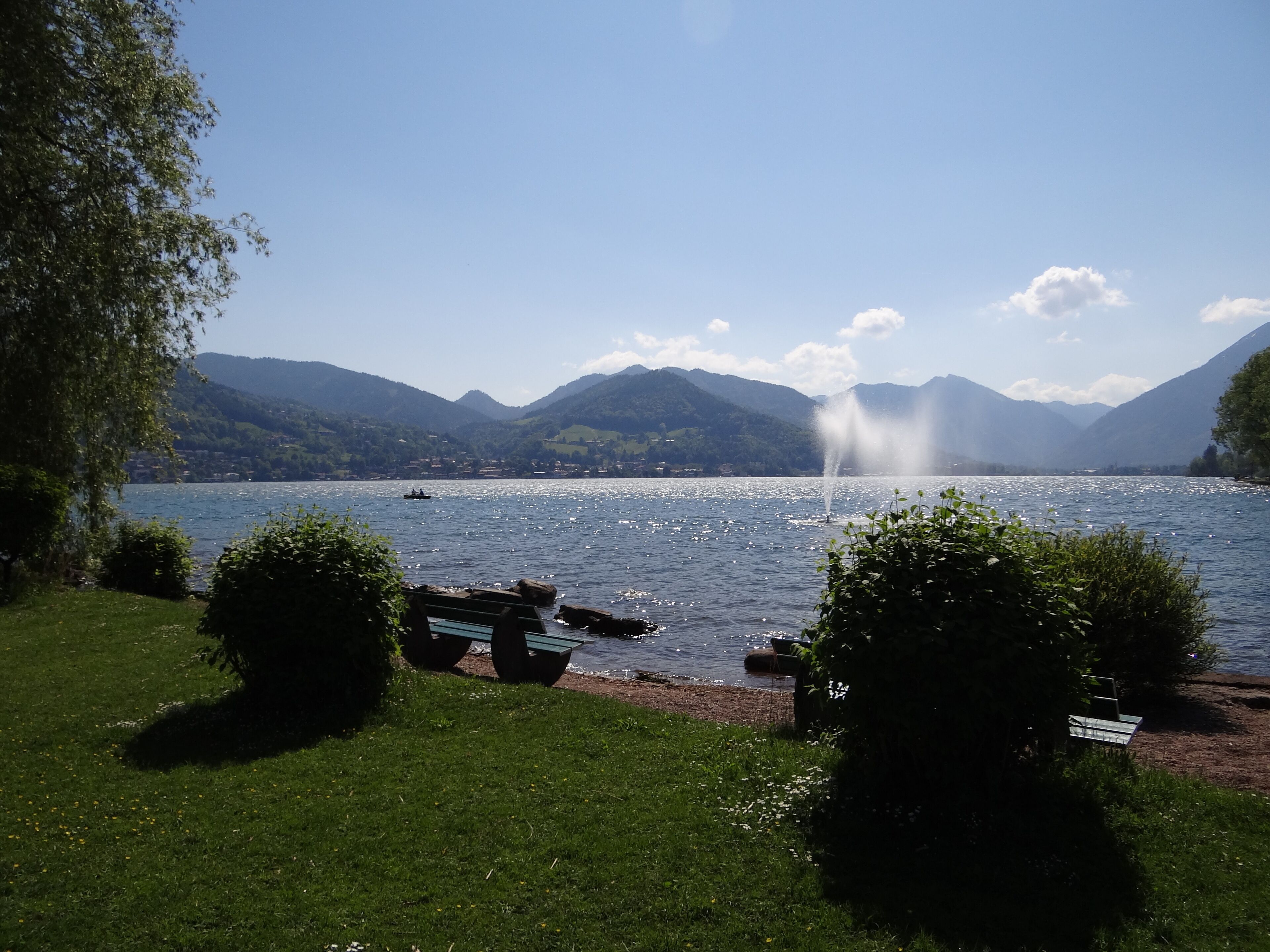 A lake with a fountain, surrounded by mountains and greenery.