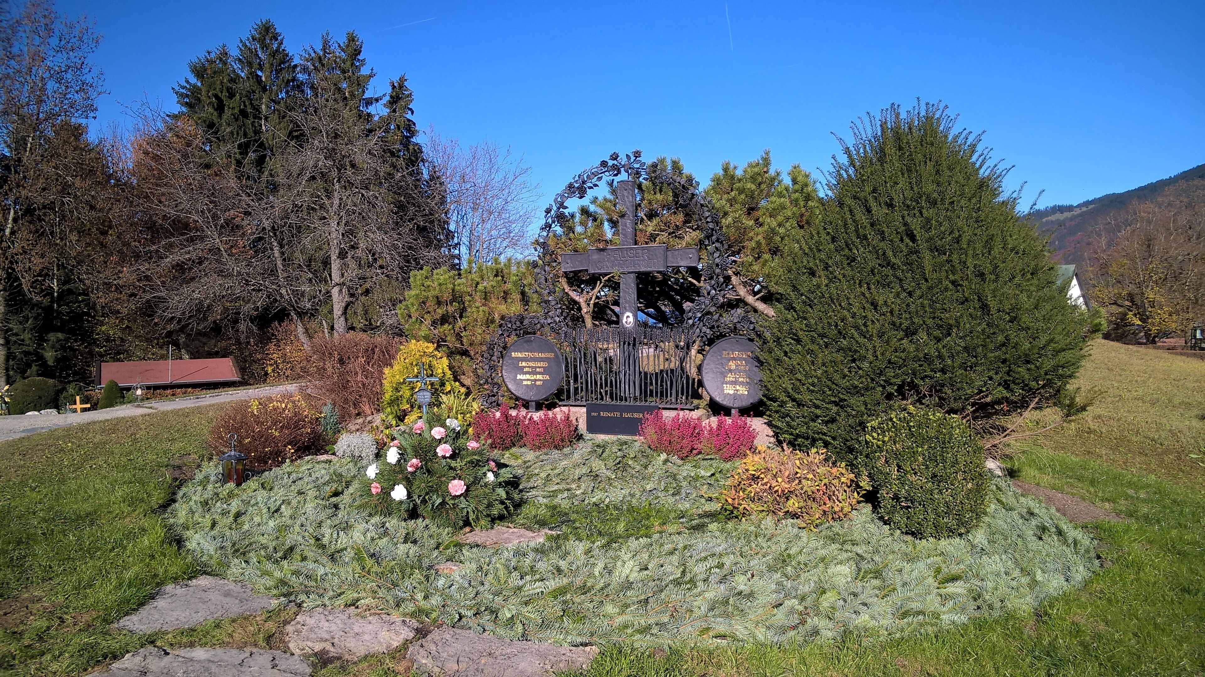 A cemetery with a cross monument surrounded by flowers and trees.