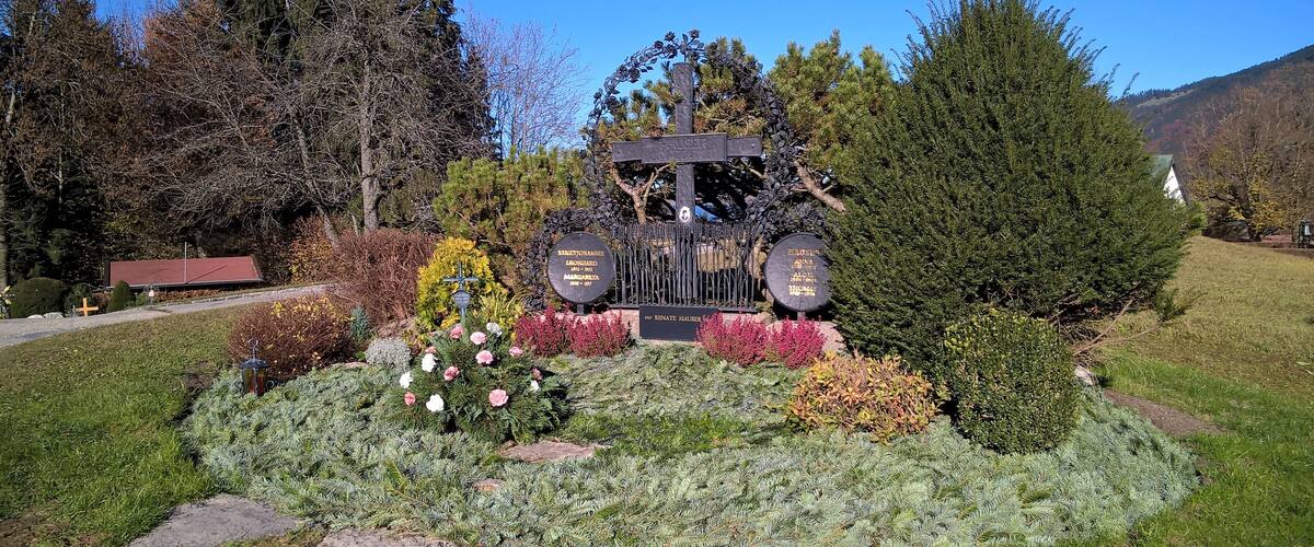 A cemetery with a cross monument surrounded by flowers and trees.