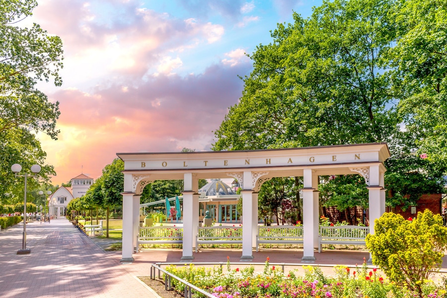 Een witte paviljoen met de tekst 'BOLTENHAGEN', omringd door een tuin met verschillende bloemen en bomen.