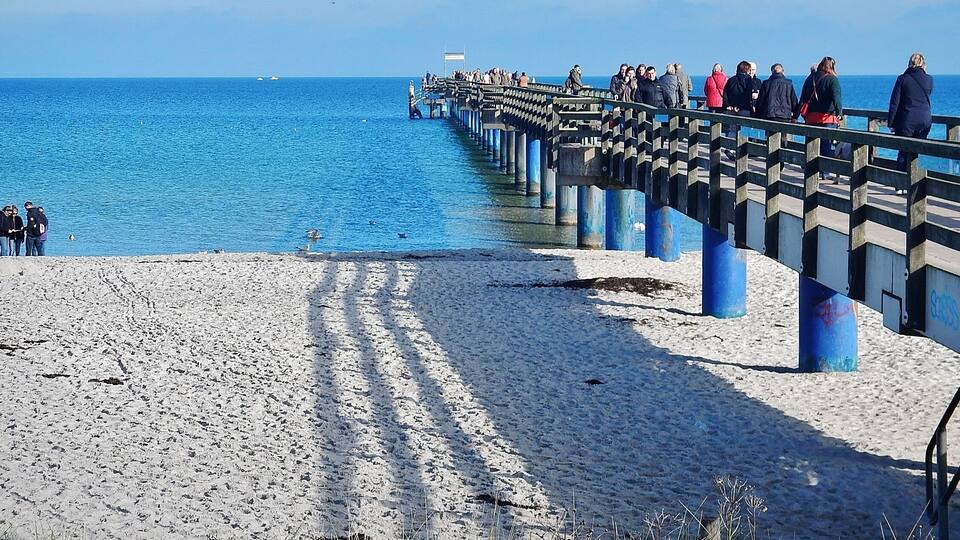 A pier extending into a calm sea with people walking along it.