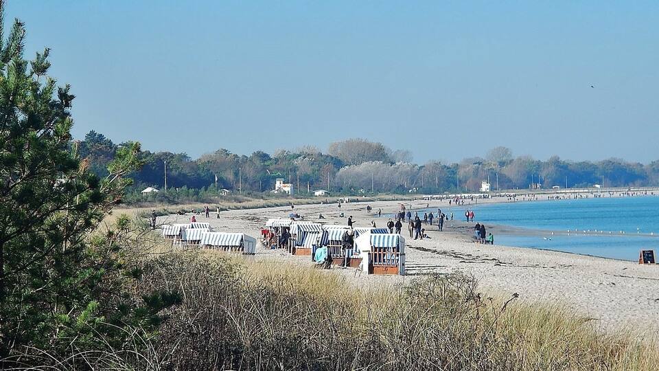 A beach with beach huts and people walking along the shore.