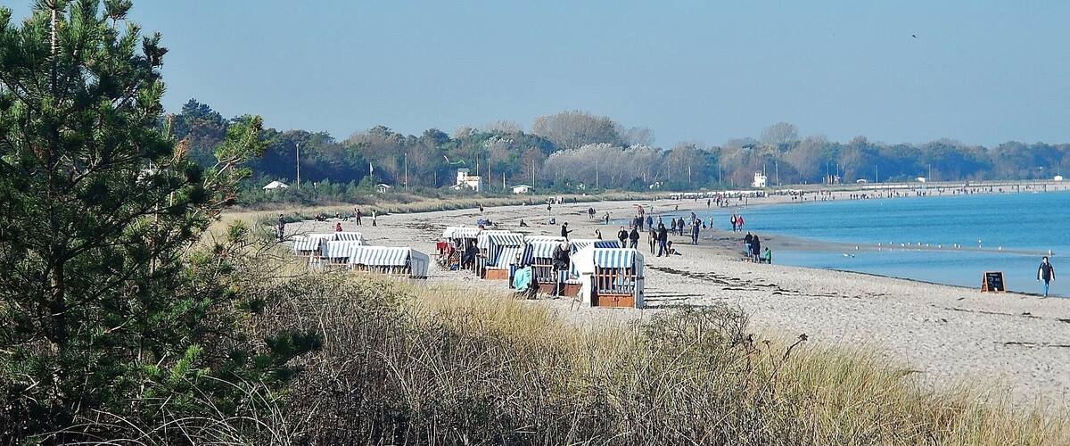 A beach with beach huts and people walking along the shore.