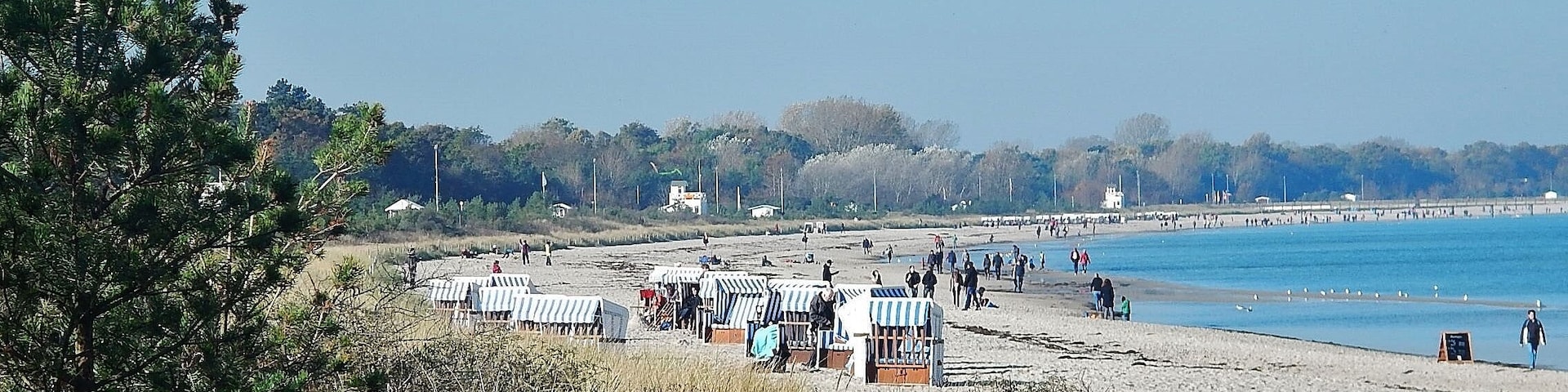 A beach with beach huts and people walking along the shore.