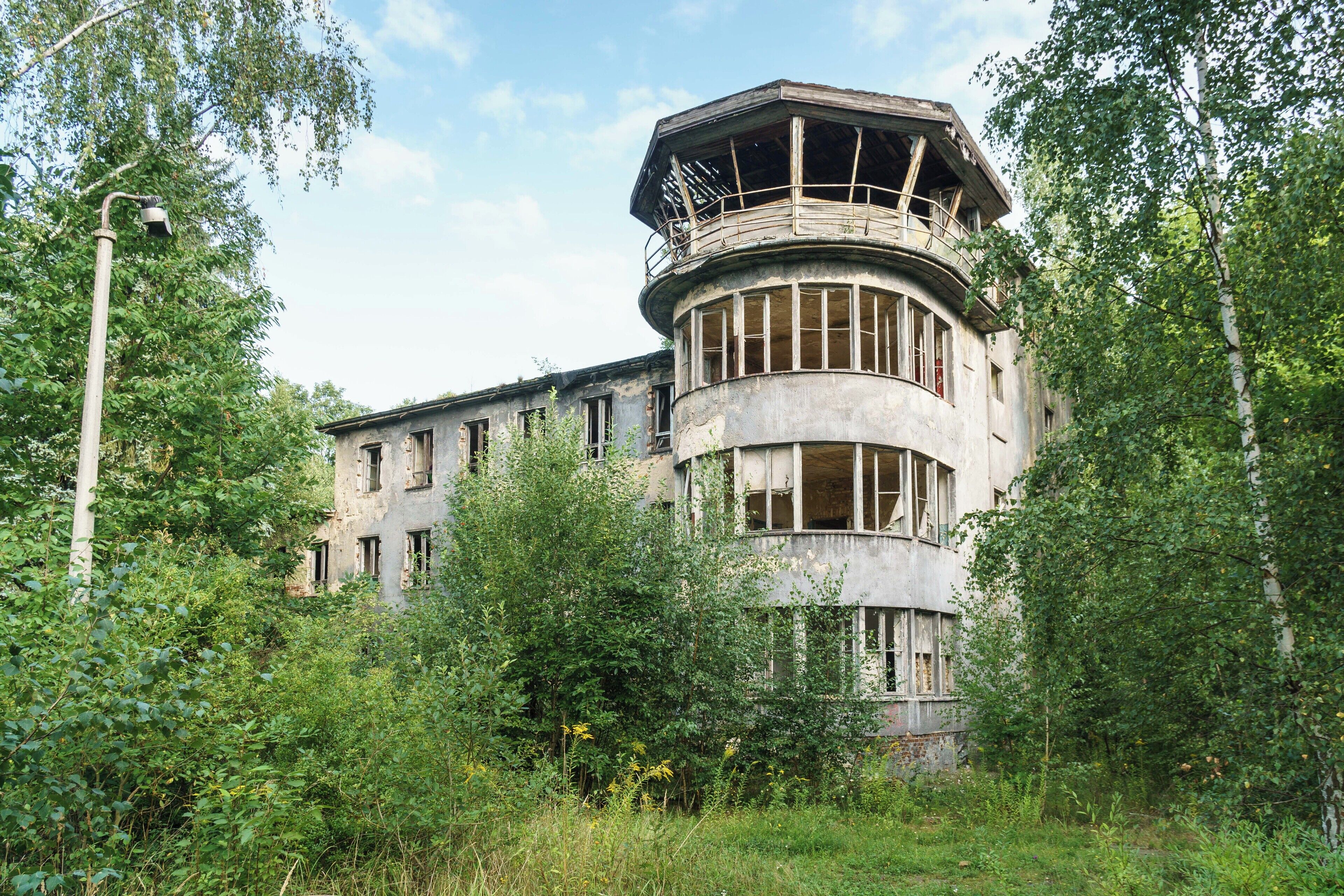 A large, circular building with a balcony, surrounded by dense greenery.