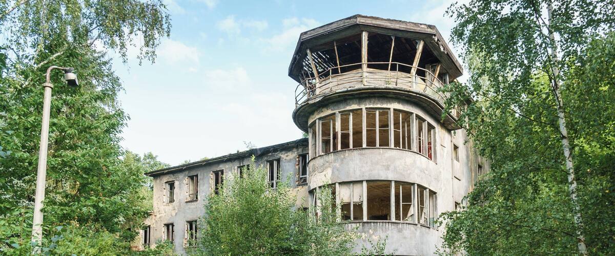 A large, circular building with a balcony, surrounded by dense greenery.