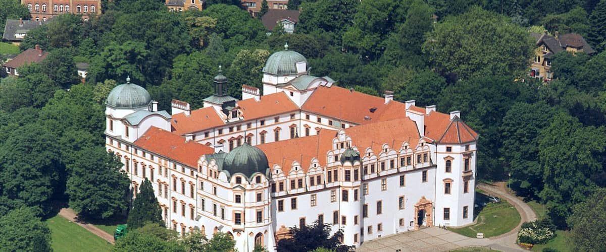 An ornate white building with red roofs surrounded by lush greenery.