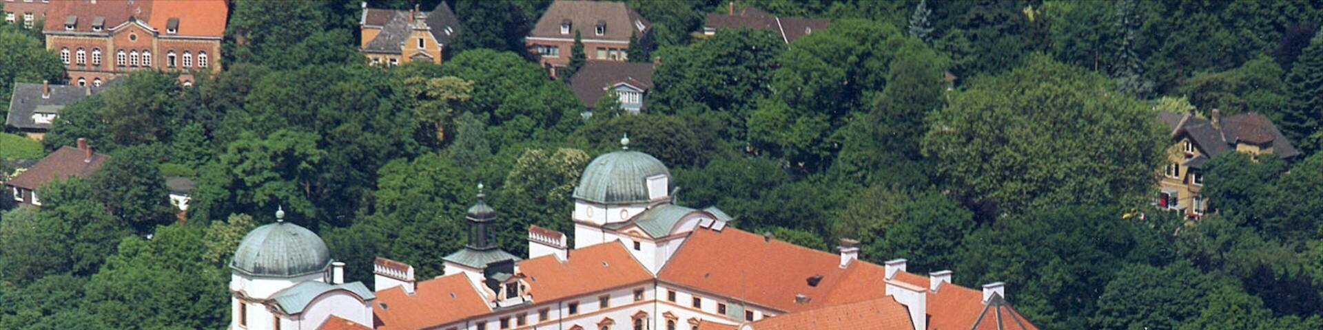 An ornate white building with red roofs surrounded by lush greenery.