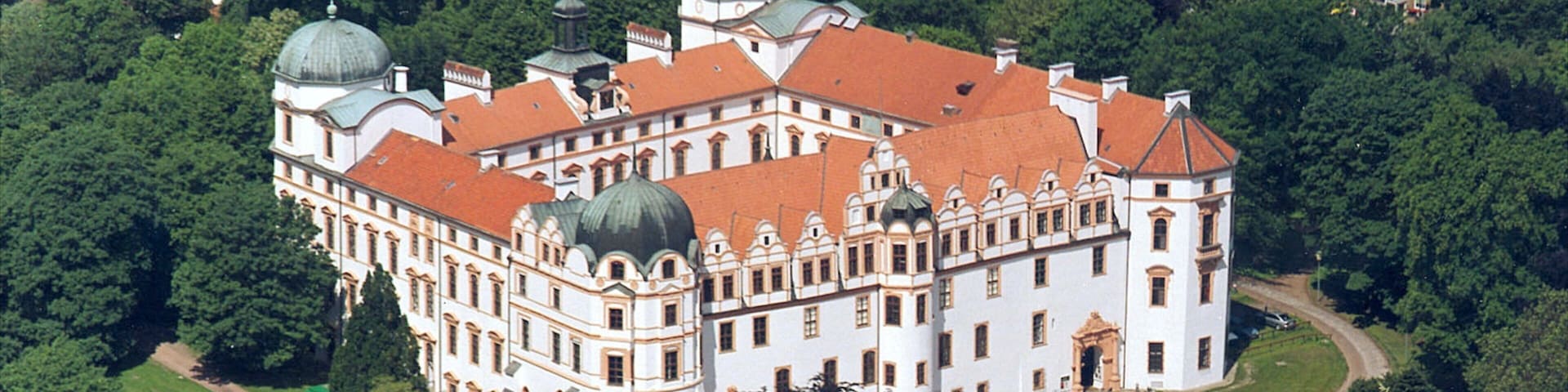 An ornate white building with red roofs surrounded by lush greenery.