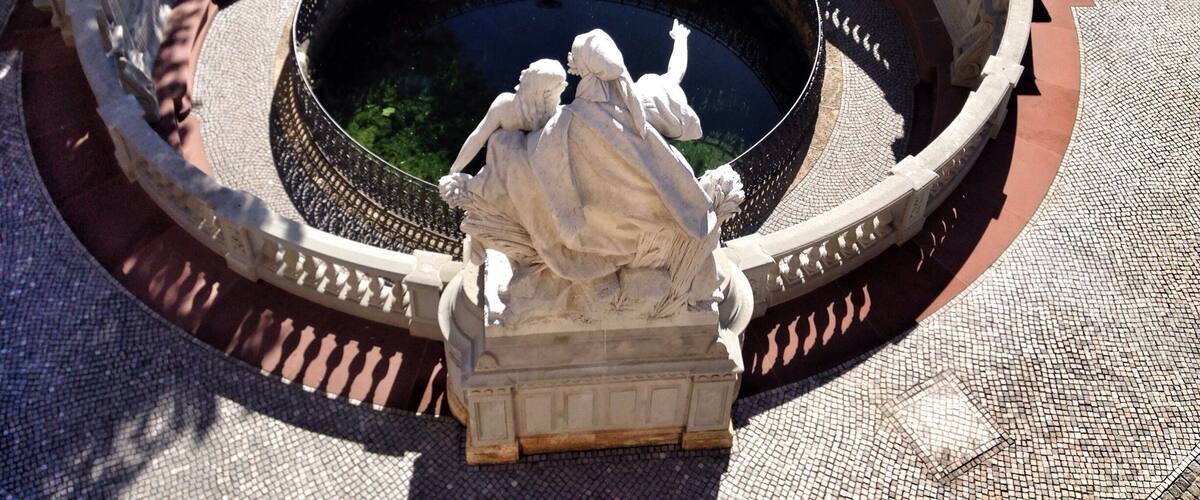 A circular fountain with a statue in the center, surrounded by a stone balustrade.