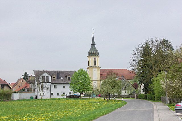 A church with a tall tower, a road, and a green field with yellow flowers.