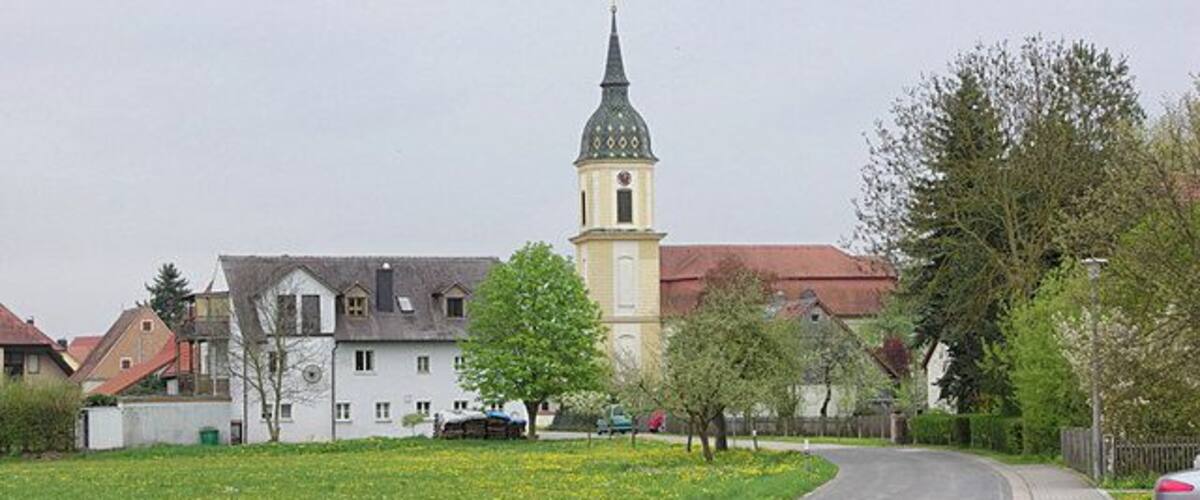 A church with a tall tower, a road, and a green field with yellow flowers.