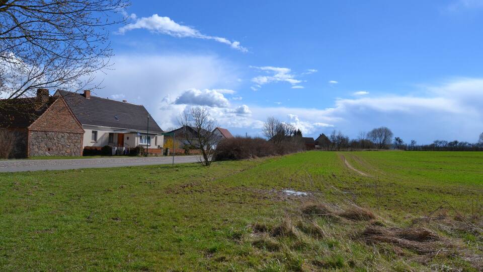 A rural landscape with houses, a grassy field, and a clear sky.