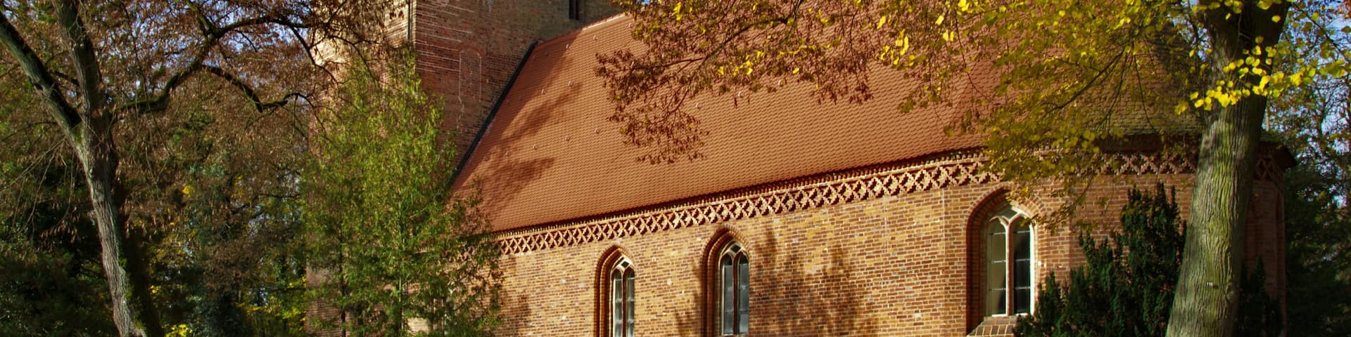 A brick church with a bell tower and a red roof, surrounded by trees with autumn leaves.