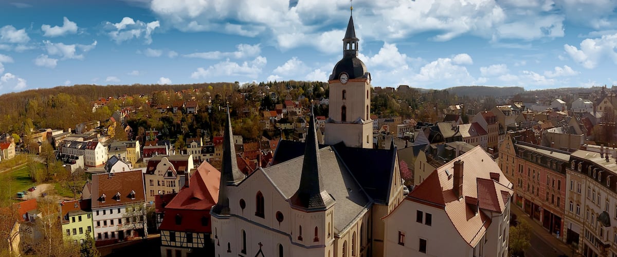 A town with a prominent church tower, colorful buildings, and a hilly backdrop.