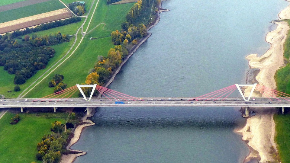 A bridge over a river with green fields and a sandy bank.