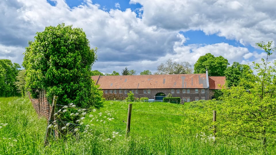 A large brick building with a red roof, surrounded by lush green fields and trees.