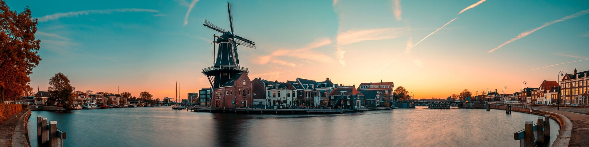 Un río tranquilo con un molino y edificios históricos al atardecer.