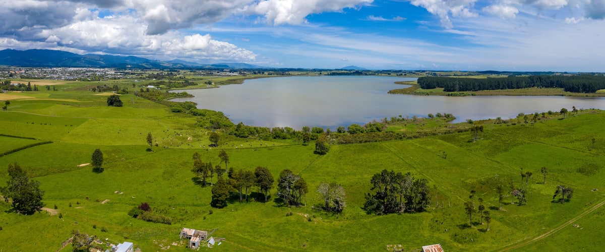 A large lake surrounded by green fields and trees, with mountains in the background.