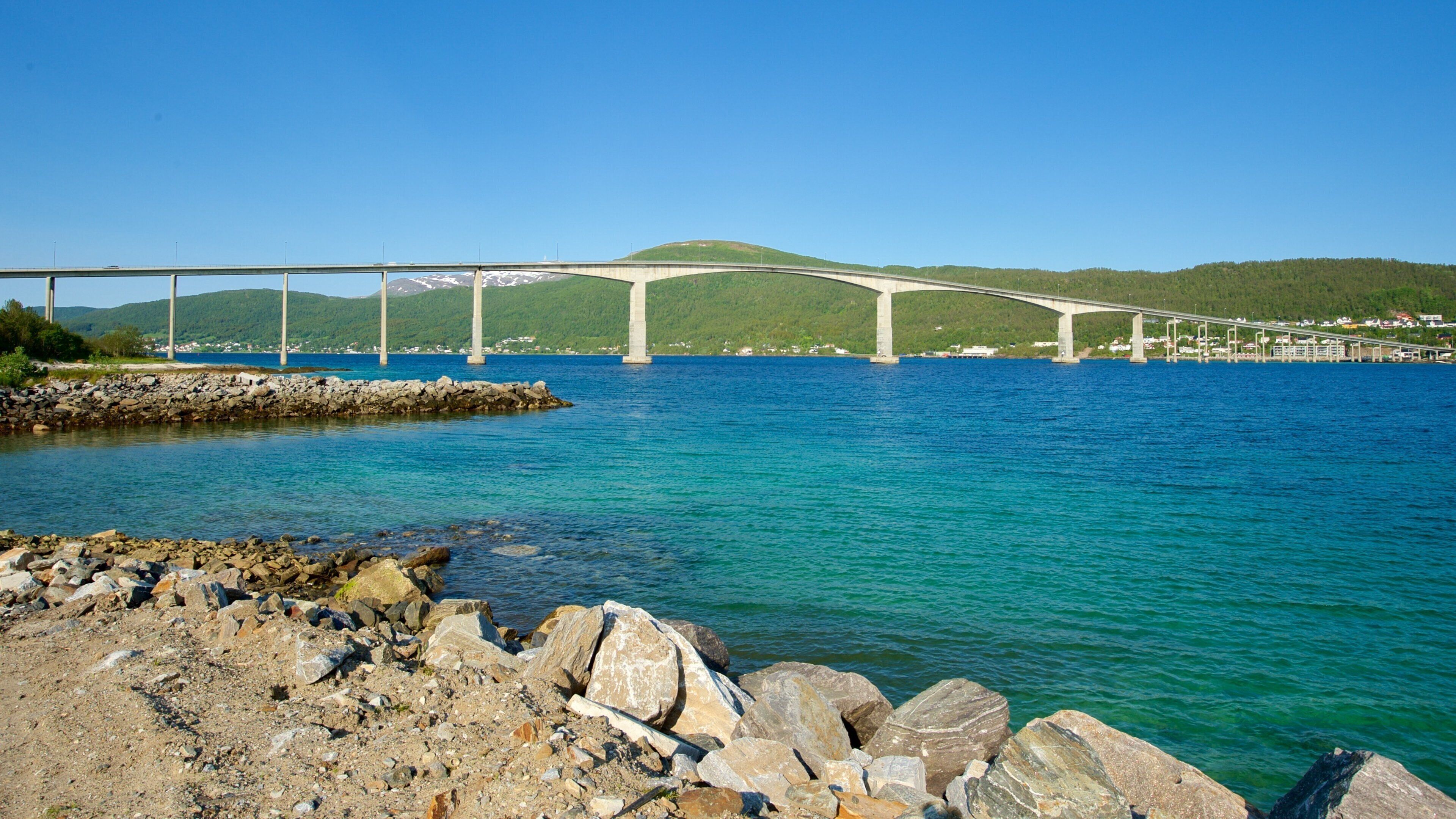 A bridge over a calm body of water with a rocky shoreline in the foreground.