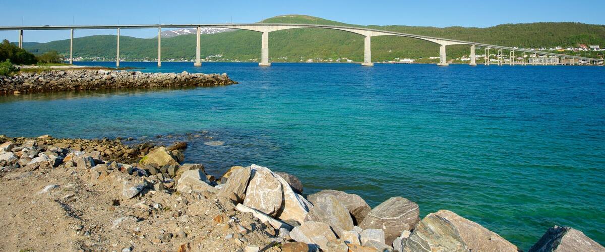A bridge over a calm body of water with a rocky shoreline in the foreground.