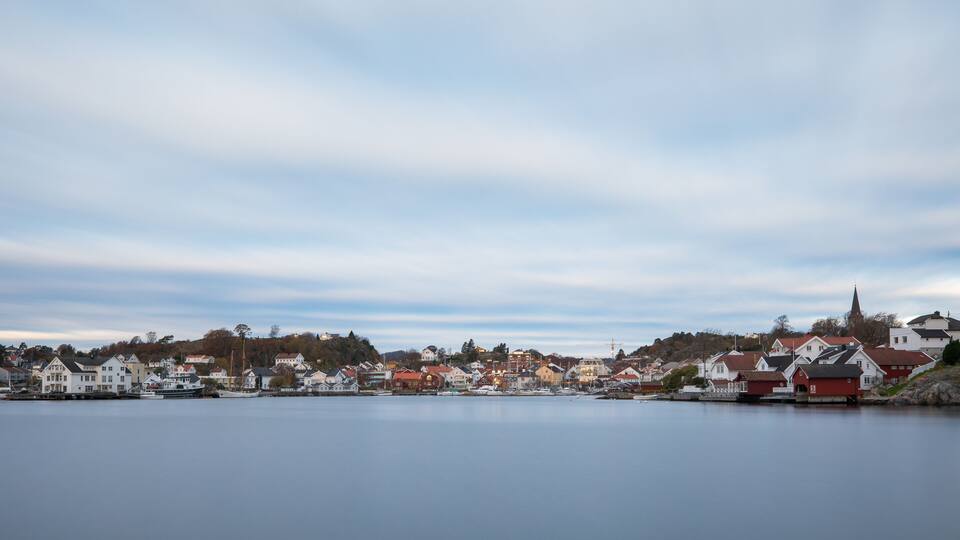 A calm lake with houses and a church steeple in the distance.