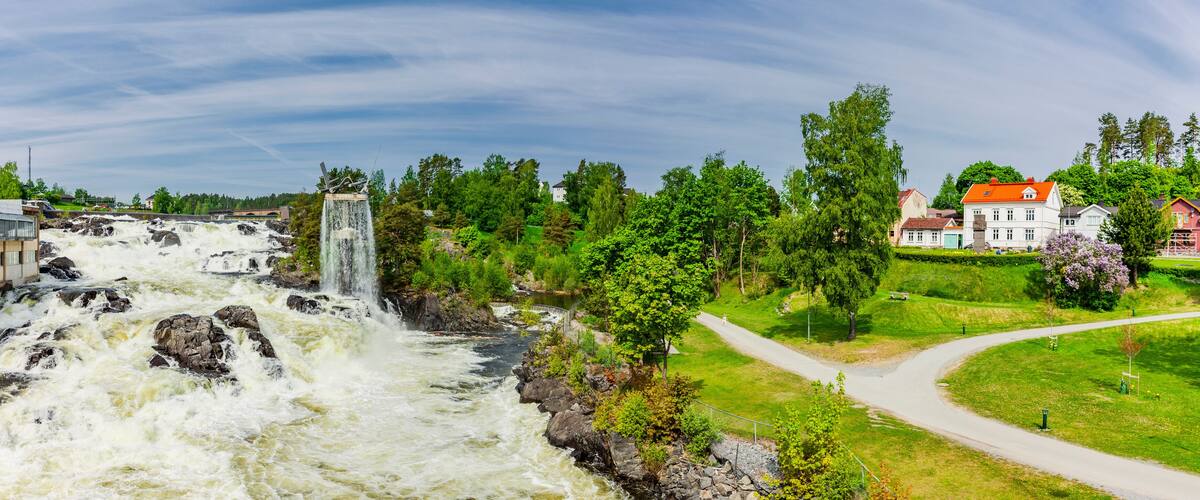 A waterfall, a river, a bridge, and houses in a green landscape.