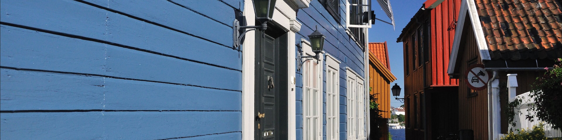 A cobblestone street with blue and red buildings, a wooden door, and a no parking sign.