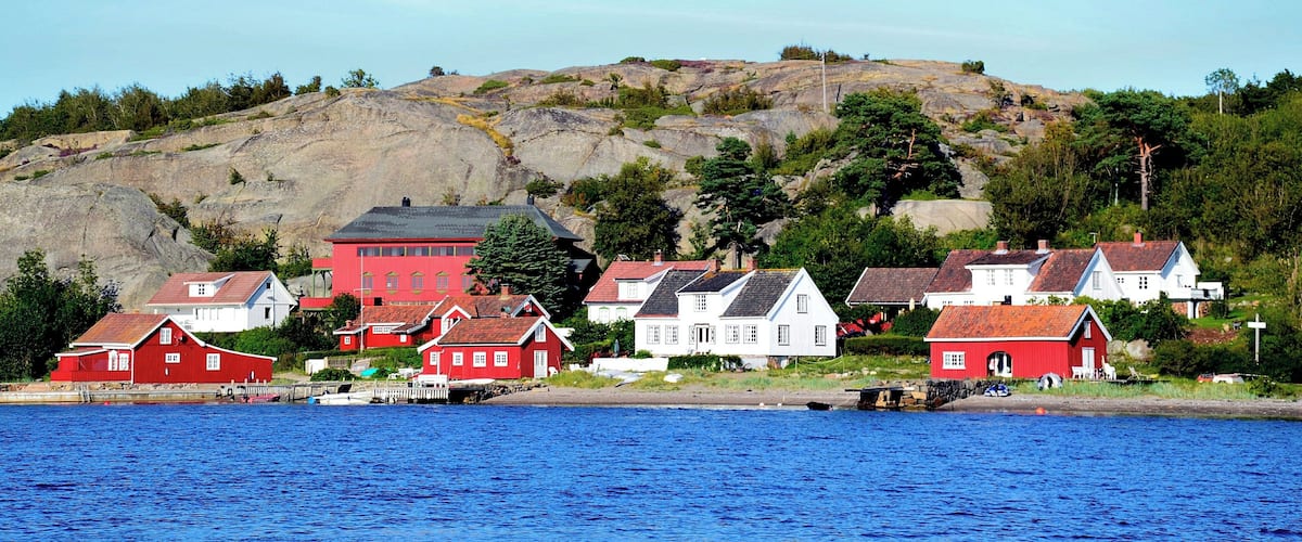 A coastal village with red and white houses, a rocky hill, and a body of water.