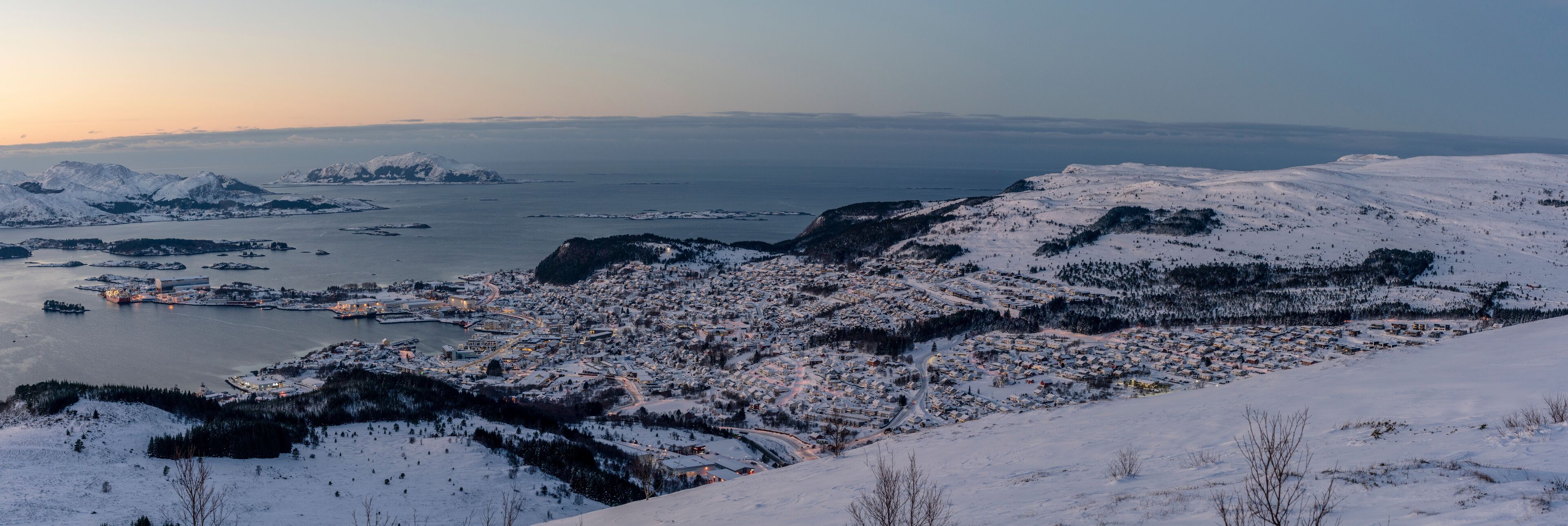 A snow-covered town with a fjord and mountains in the background.