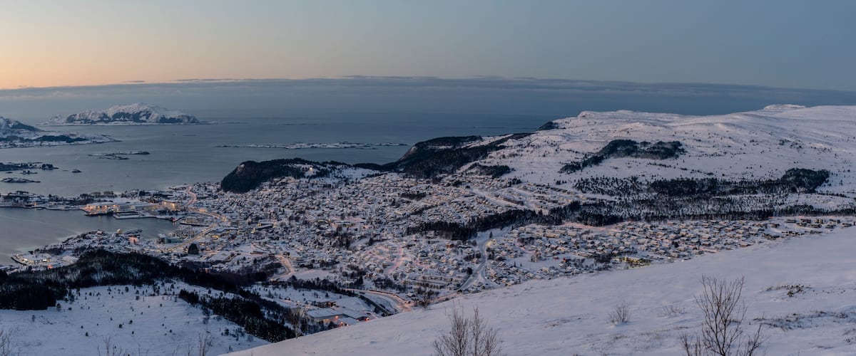 A snow-covered town with a fjord and mountains in the background.
