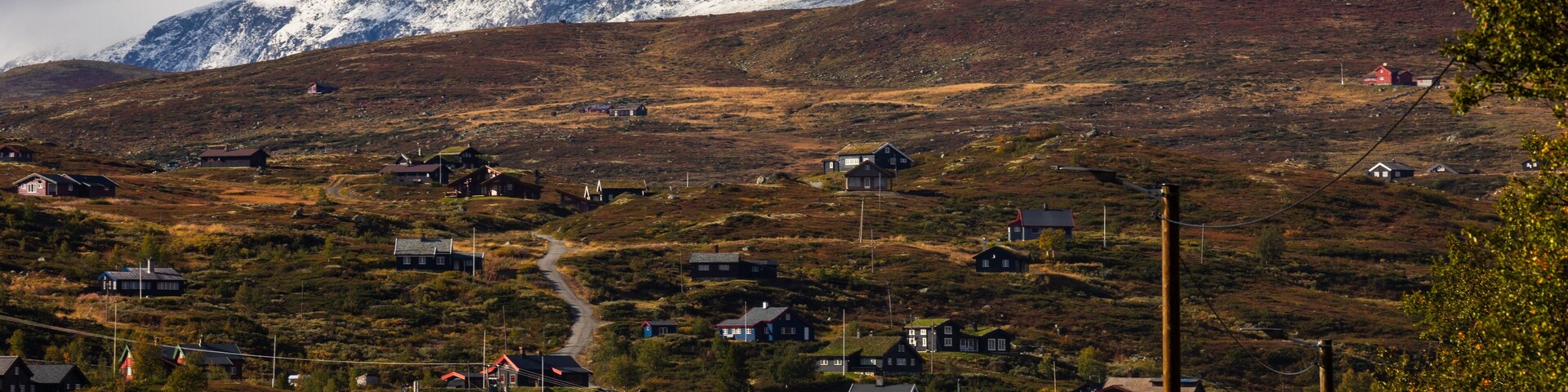 A rural landscape with scattered houses, a winding road, and snow-capped mountains in the background.