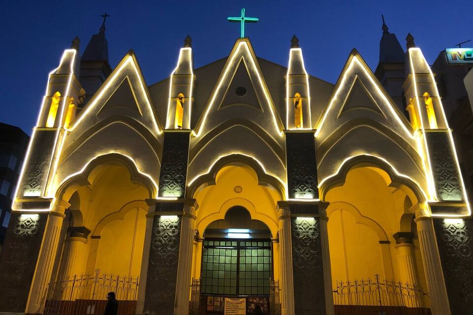 A church with a cross on top, illuminated arches, and a large entrance.