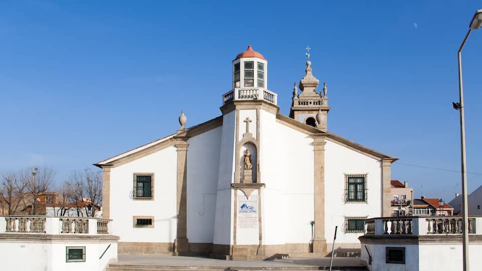 A white church with a bell tower and a statue in front.