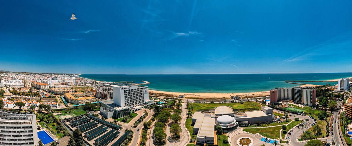 A coastal cityscape with a beach, a large stadium, and modern buildings.