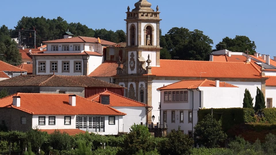 A town with red-tiled roofs, white buildings, and a prominent church with a bell tower.