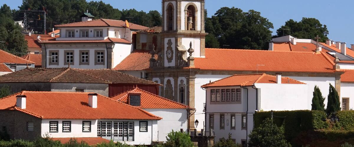 A town with red-tiled roofs, white buildings, and a prominent church with a bell tower.