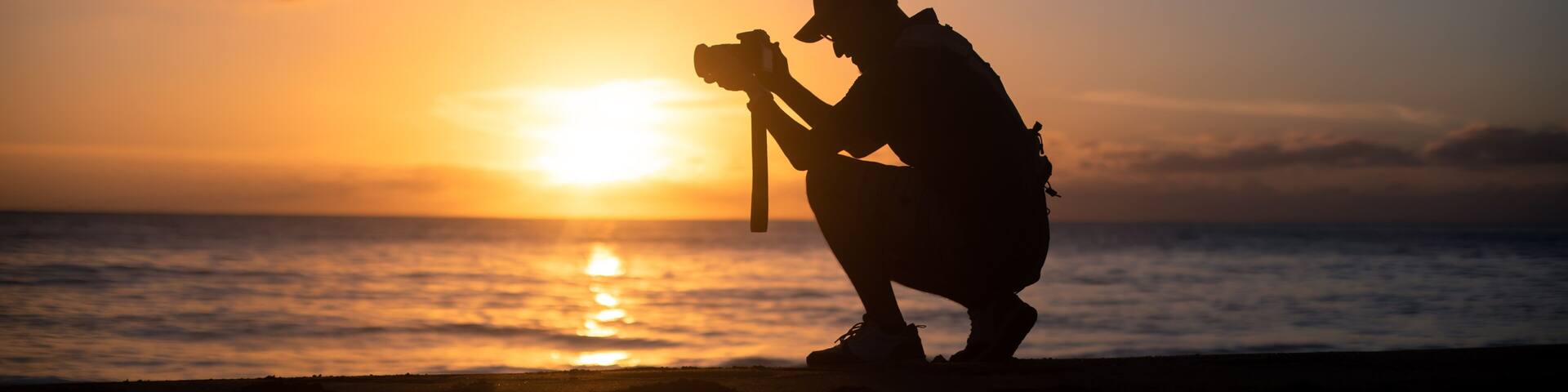 The silhouette of a male hobbyist photographer taking photos of a beautiful colorful sunset on the West Puerto Rico coast near Rincon