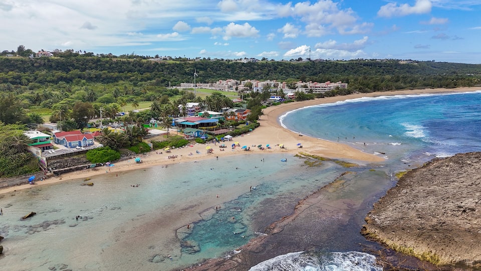 A coastal town with a beach, clear waters, and surrounding greenery.