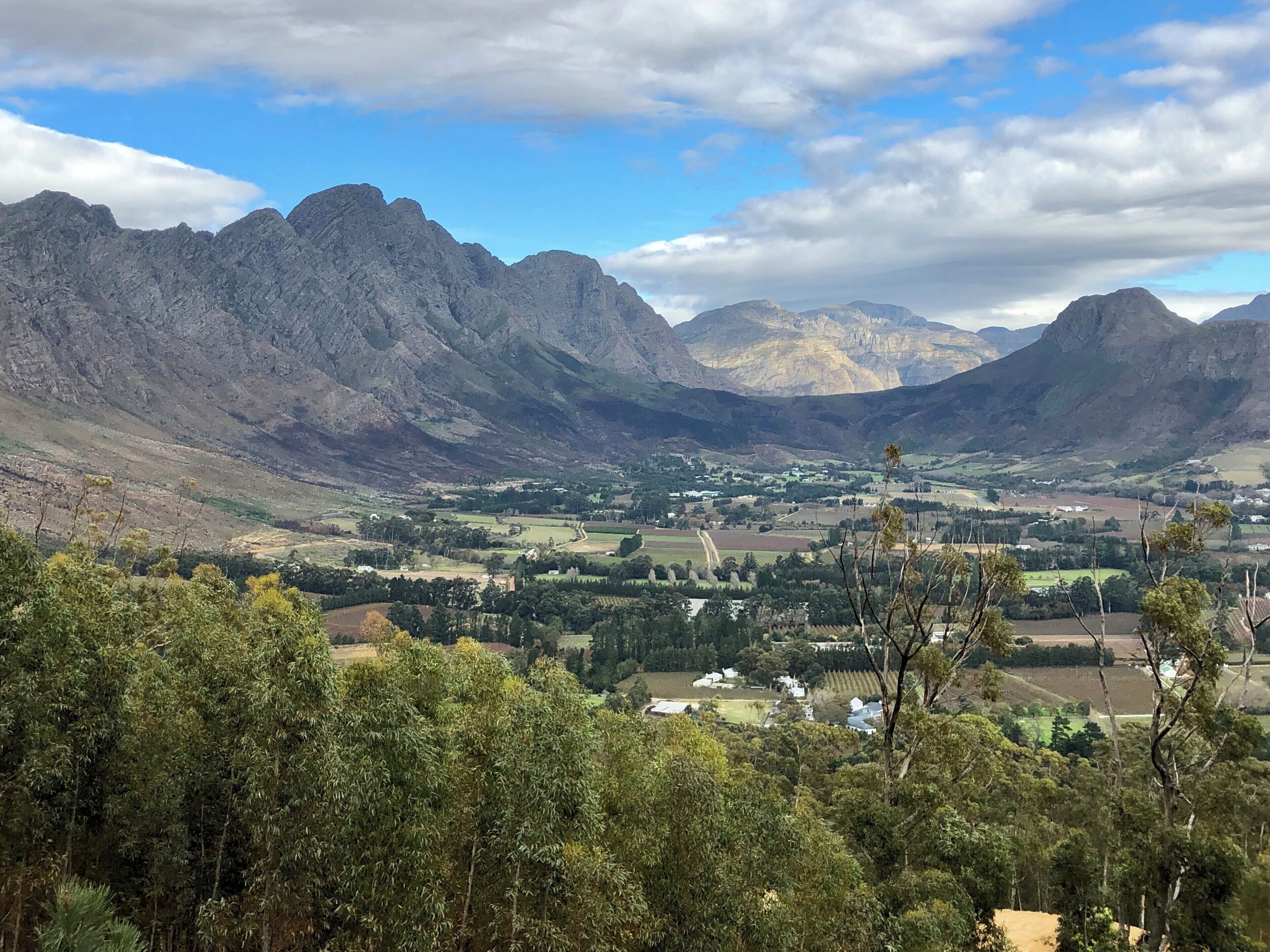A mountainous landscape with a valley, scattered houses, and dense green trees.
