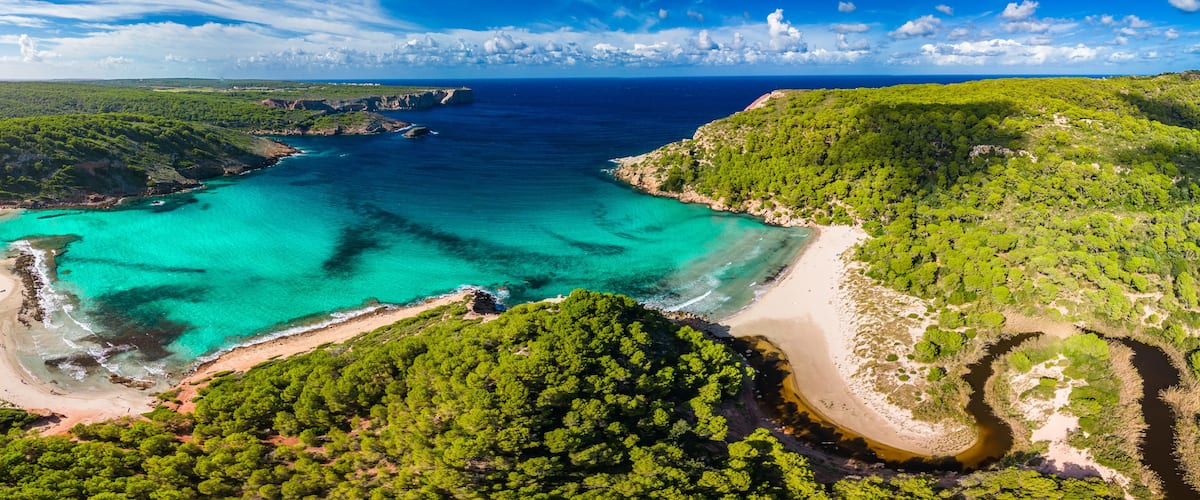 A coastal landscape with turquoise waters, a sandy beach, and dense green forests.