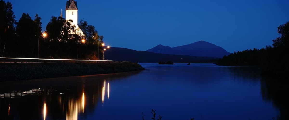 A church with a spire, a calm lake, and a mountain in the background.