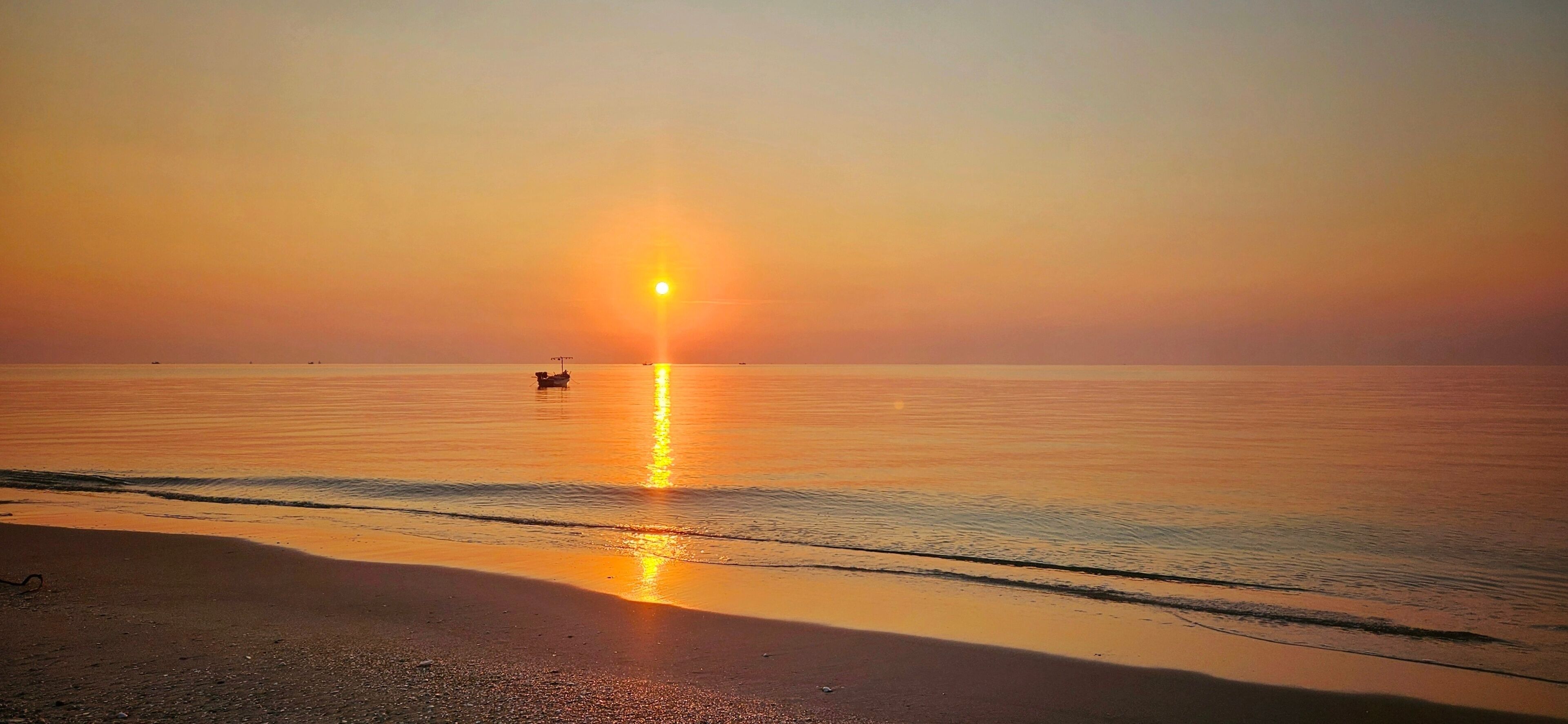 A sunset over a calm sea with a boat in the distance.