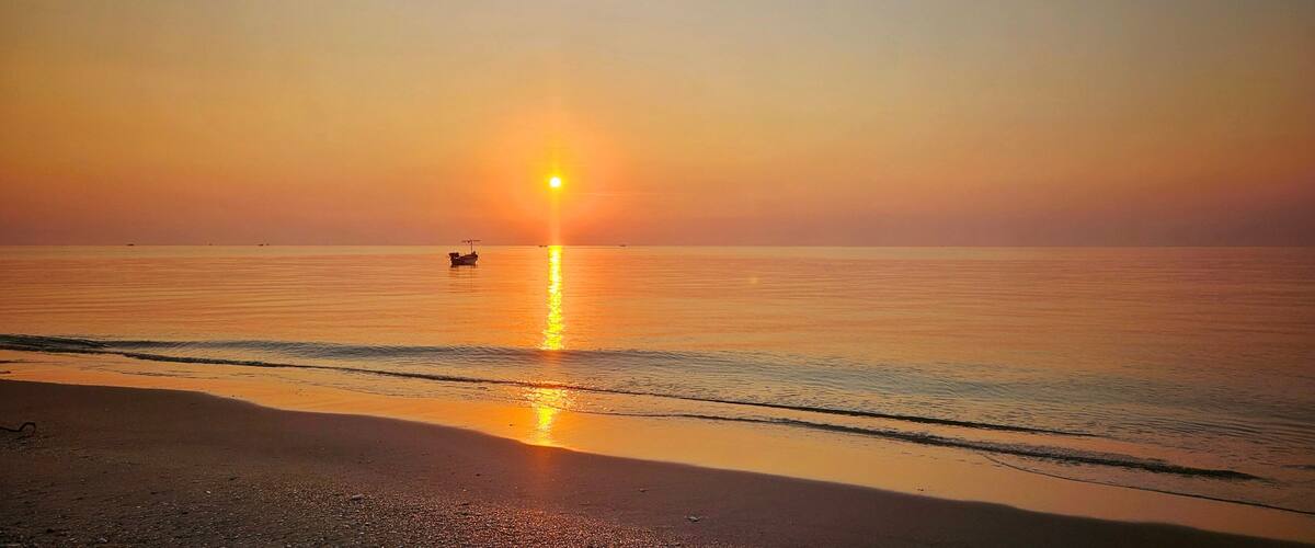 A sunset over a calm sea with a boat in the distance.