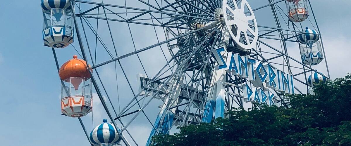 A large Ferris wheel with blue and white gondolas and orange cabins, surrounded by trees.