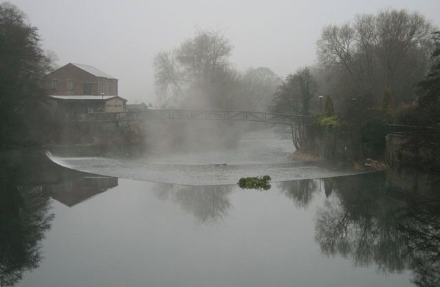 A foggy river with a bridge and a house on the left.