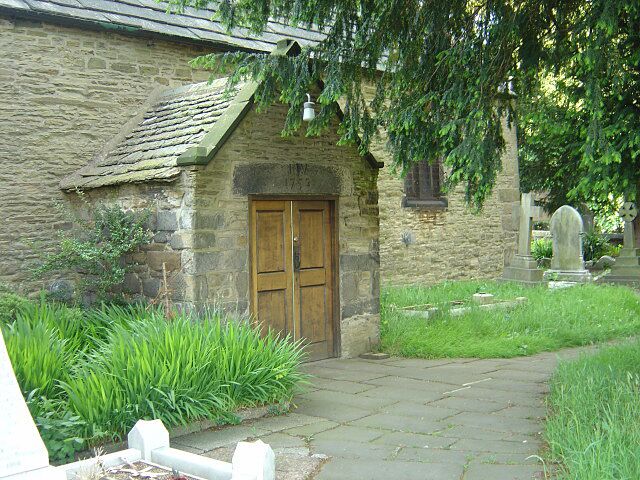 St Luke's Church, Heage Porch on the south side of the old wing of the church. Heage Parish Church has a most unusual T-shaped layout. This view shows the older part of the church which forms the upright of the T and is aligned more or less east-west. The lintel over the porch doorway is inscribed JW 1752. The church was originally built of wood, but was destroyed by a violent tempest in June 1545. Rebuilt in 1661, it was enlarged in 1836 Trees make it impossible to show what this church really looks like.