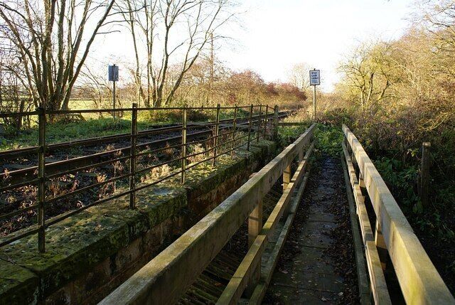 A railway track with a wooden fence and a signpost in a rural setting.