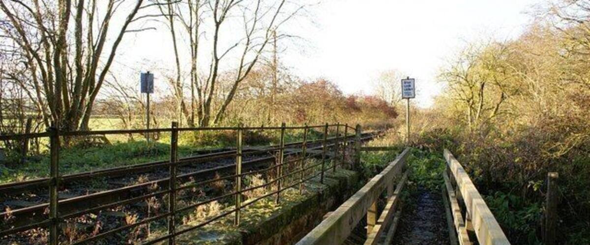 A railway track with a wooden fence and a signpost in a rural setting.