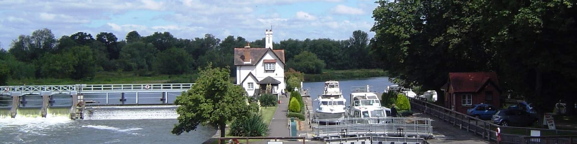 A riverside scene with a white house, boats, and a bridge.